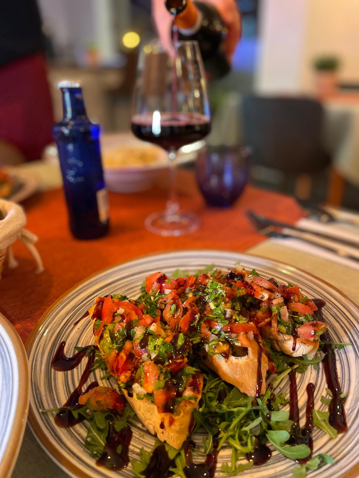 Bruschetta auf einem Teller mit einem Glas Wein im Hintergrund